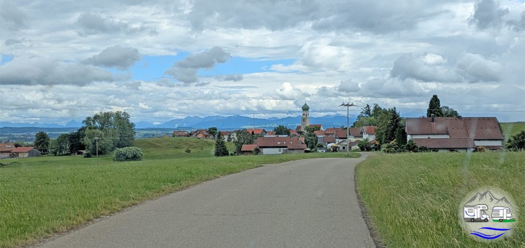 Ausblick auf ein Allgäuer Dorf mit Kirche und Bergpanorama im Hintergrund