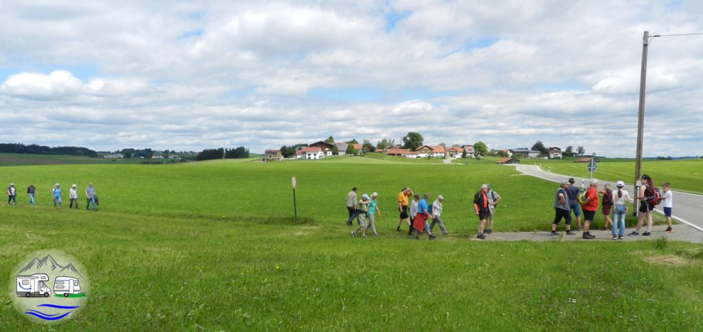 Familiengruppe wandert auf einem Feldweg durch grüne Wiesen im Allgäu