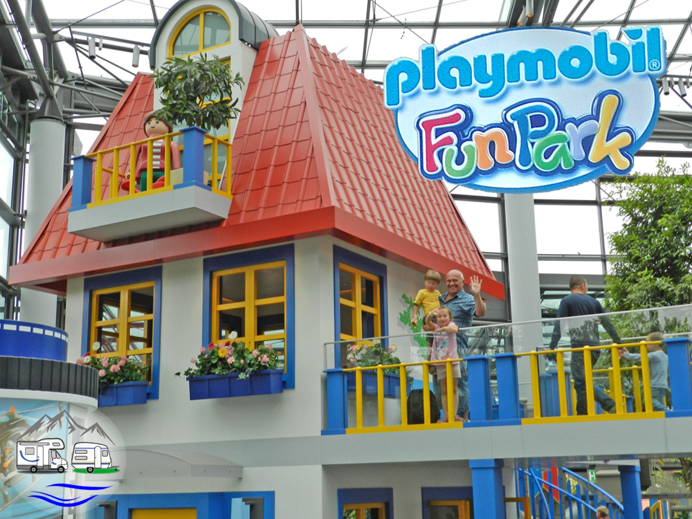 Blau-gelbes Playmobil-Haus mit Playmobil-Funpark-Logo, Besucher winken von einem Balkon