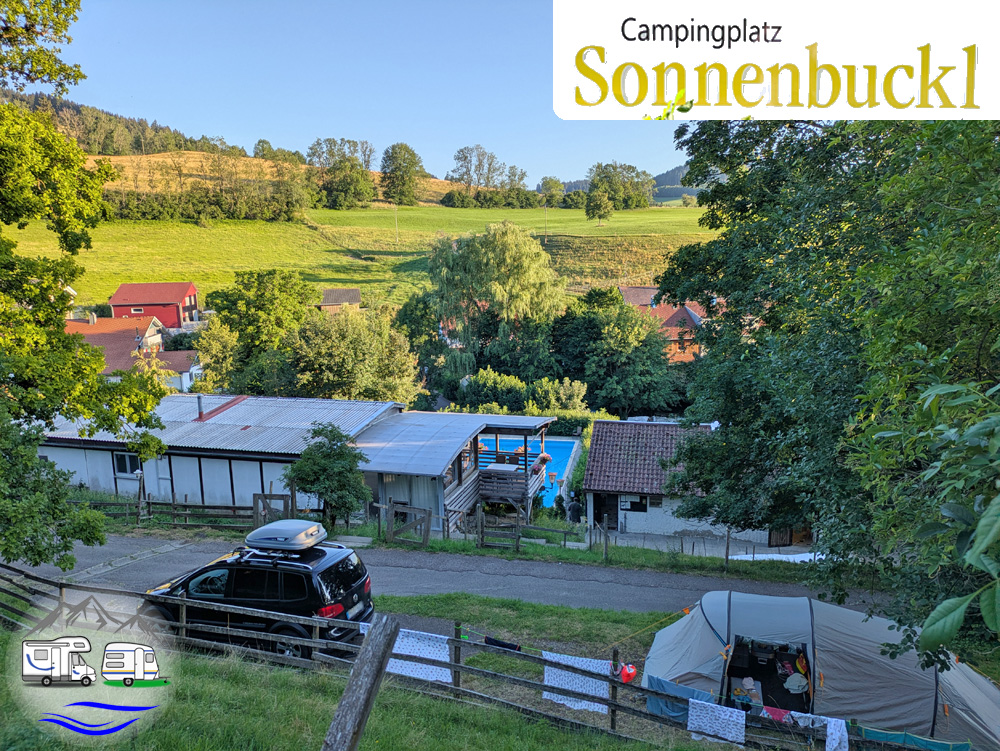 Stellplätze auf dem Campingplatz Sonnenbuckl mit Auto, Zelt und Pool, im Hintergrund grüne Hügel und ein Dorf